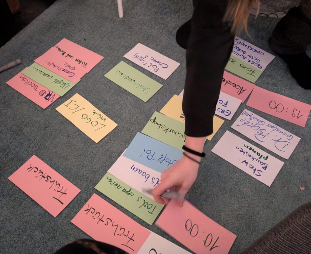 Jemand sortiert Bunte rechteckige Zettel auf dem TeppichfuĂboden. Auf den Zettel stehen verschiedene AktivitĂ€ten