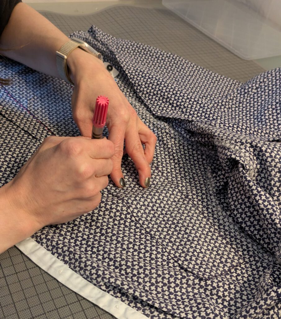 Auf einem StĂŒck Stoff wird mit einem pinken Filzstift eine Schablone markiert