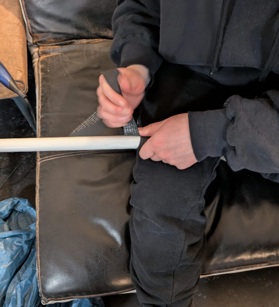 Eine Person wickelt ein dunkles Band um einen Stab