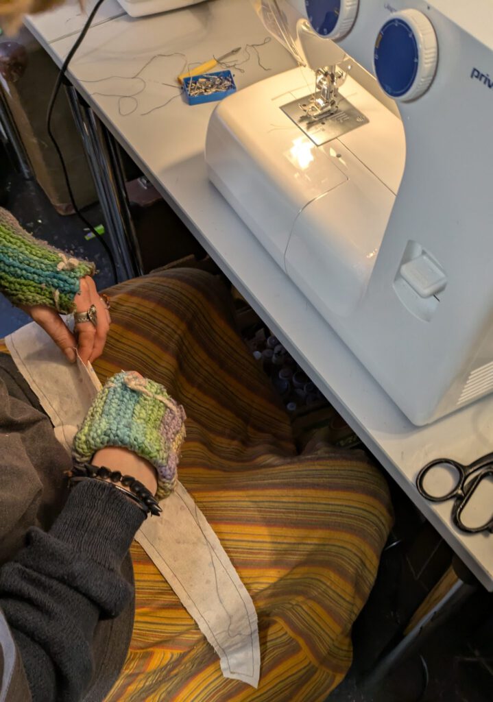 Jemand sitz vor einer NĂ€hmaschine und bereite auf dem Schoss Stoffteile vor