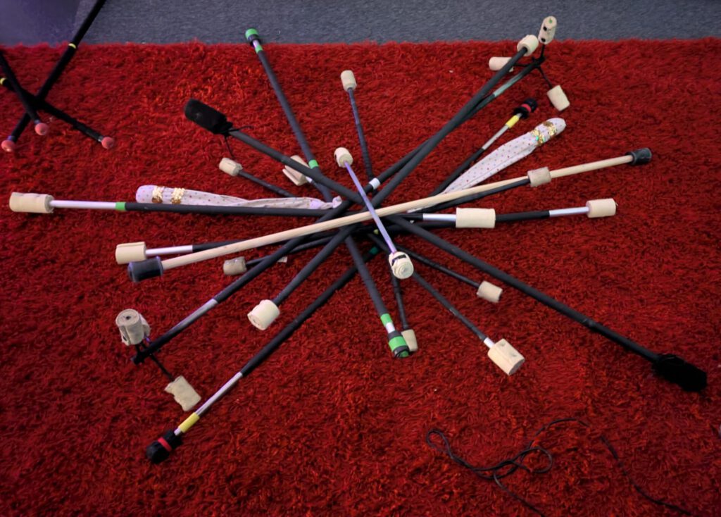 Viele JonglierstĂ€be liegen zentral gekreuzt ĂŒbereinander. Zusammen liegen sie auf einem roten flauschigen Teppich