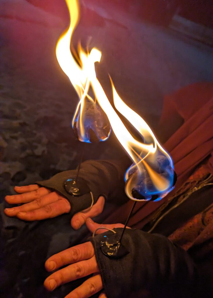 Zwei hell brennende Koten sitzen auf einem Draht. Der Draht ist am Ende an zwei HĂ€nden befestigt, es sind sogenannte Candles zum Feuer spielne