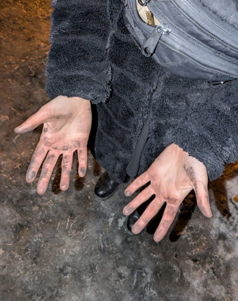 Eine Person zeigt ihre HĂ€nde, die sind voll schwarzem RuĂ