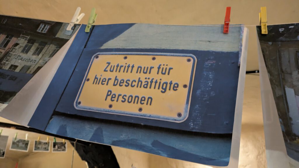 ein ausgedrucktes Foto an einer Wäscheleine, darauf ein Hinweisschild in gelb mit schwarzer Schrift "Zutritt nur für hier beschäftigte Personen"