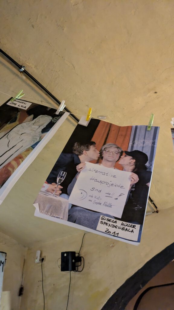 Ein ausgedrucktes Foto an einer Wäscheleine, darauf küssen zwei Personen von links und recht einer älteren lächelnden Person, Gisela Müller, die Wangen